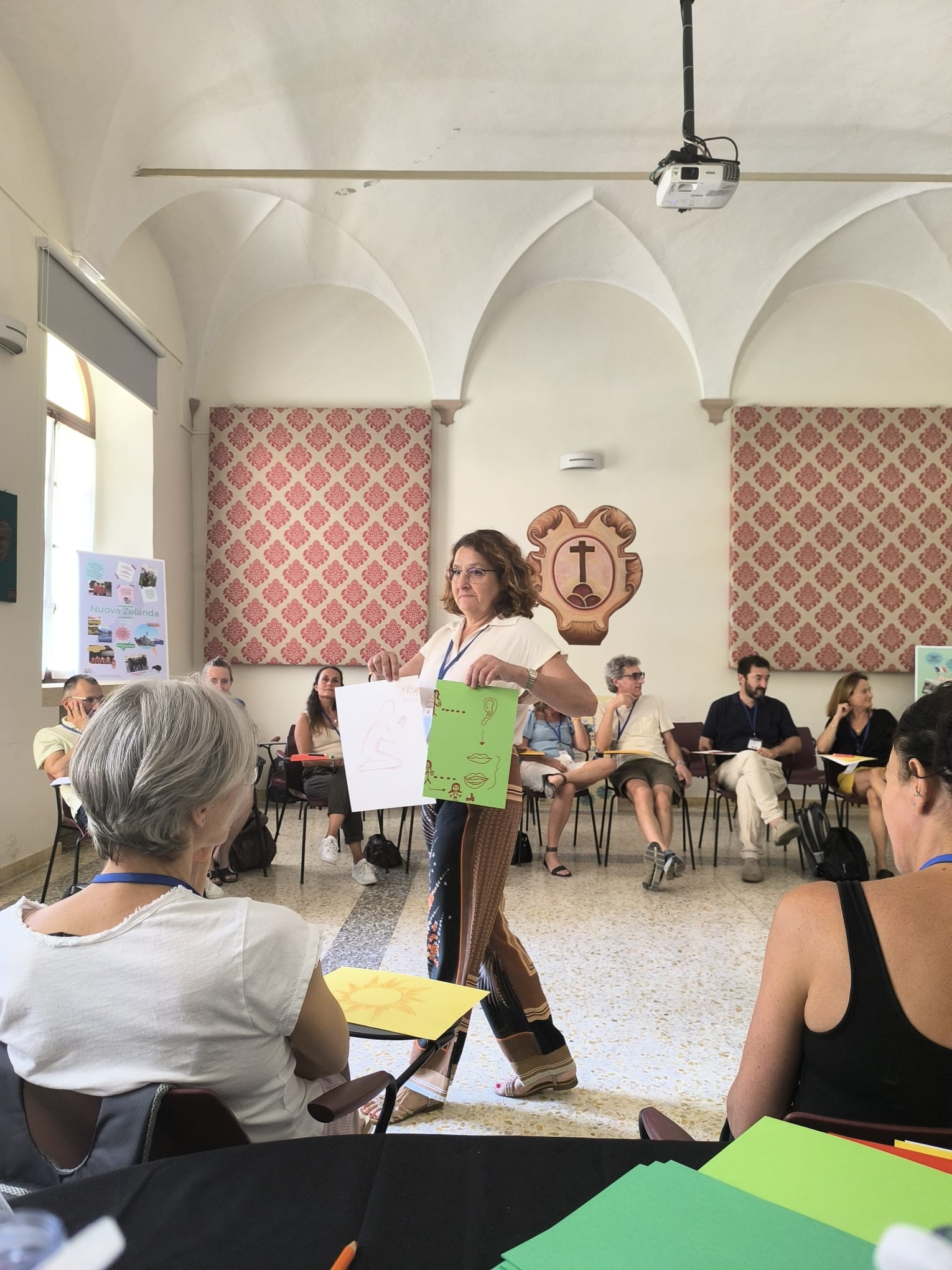 Cristina Zucchi mostra due elaborati a un gruppo di adulti seduti in cerchio durante un laboratorio di formazione esperienziale